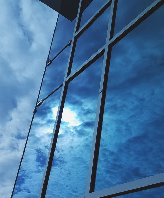 Windows with blue sky, clouds, and sun reflecting off them.